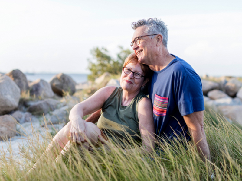 A happy couple sitting in the grass on the beach smiling together | Icon Cancer Centre